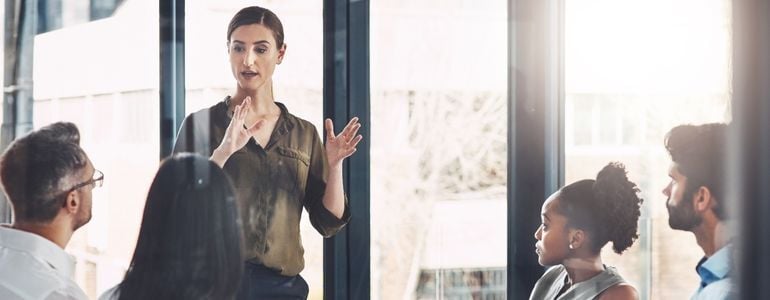 Persona dando un mensaje a un grupo de colaboradores en una oficina, practicando consejos para mejorar la comunicación ejecutiva