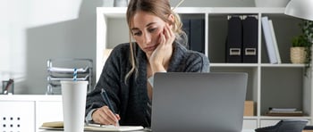 Mujer en un escritorio escribiendo con desmotivación laboral