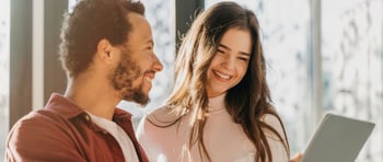 Dos jóvenes mirando a una tablet sonriendo y planeando emprender en pareja para este San Valentín