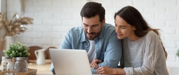 Dos jóvenes mirando a una tablet sonriendo y planeando emprender en pareja para este San Valentín