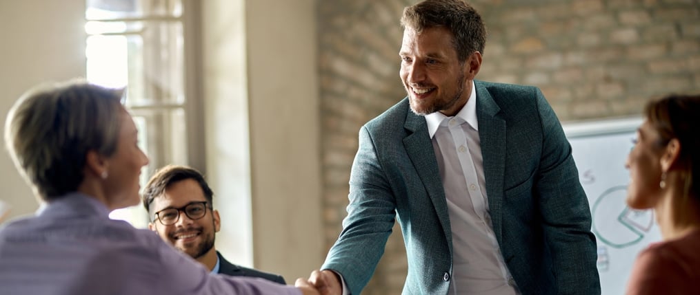 Hombre de traje estrechando la mano con una clienta tras hacer un cierre de ventas